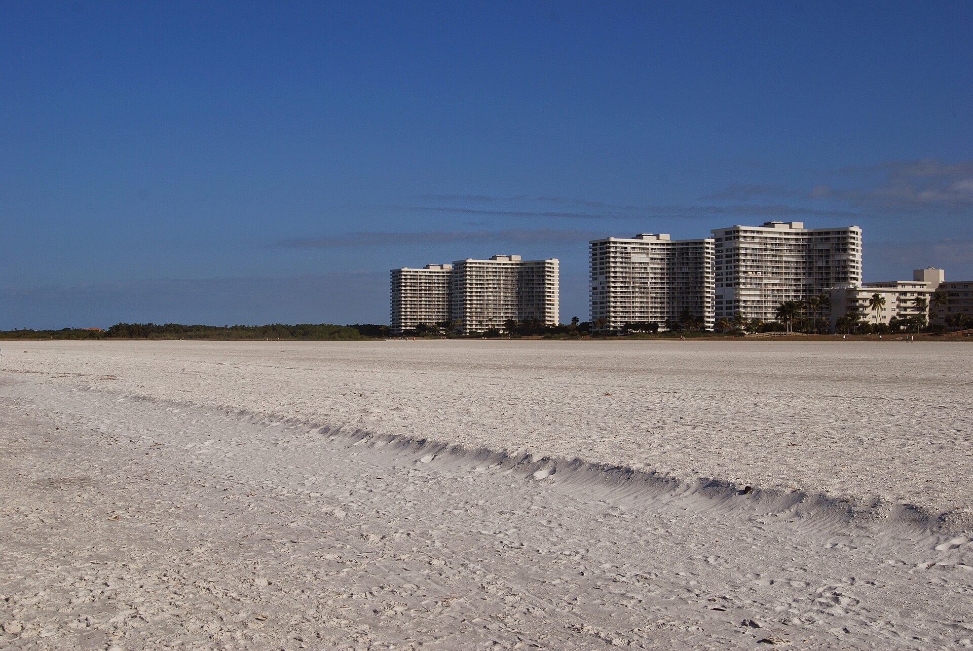 Marco Island beach with white sand and shoreline high-rises under a clear blue sky